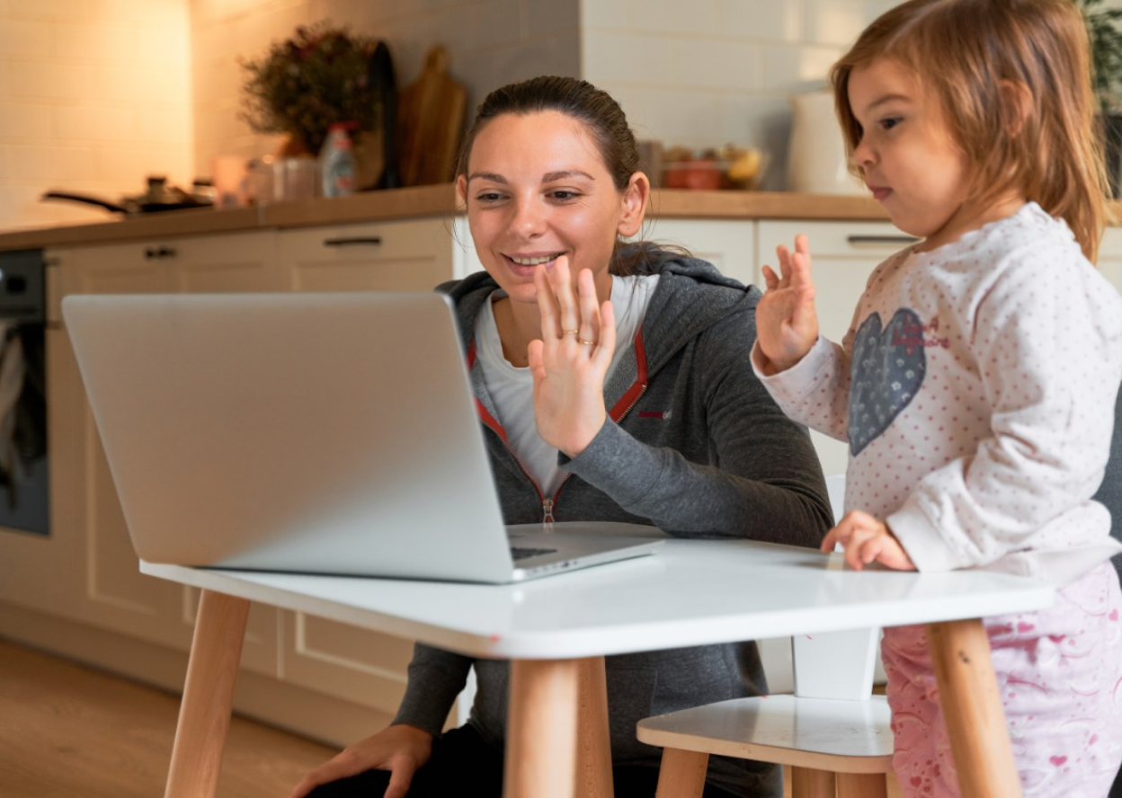 A child and guardian waving at laptop screen.
